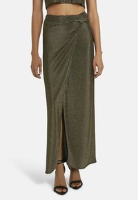 Metallic grüne Maxikleid mit einem seitlichen Schlitz, gerafftem Detail am Bund und glatter Textur. Trägt schwarze High Heels Sandalen.