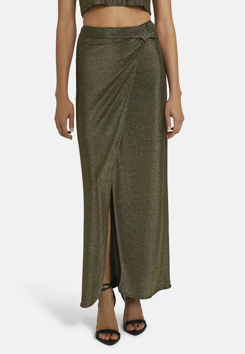 Metallic grüne Maxikleid mit einem seitlichen Schlitz, gerafftem Detail am Bund und glatter Textur. Trägt schwarze High Heels Sandalen.