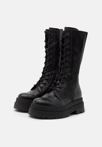 Bottes à lacets en cuir noir montant jusqu'au genou, avec une semelle plateforme épaisse et une finition texturée. Caractéristiques : 18 œillets et un design robuste.