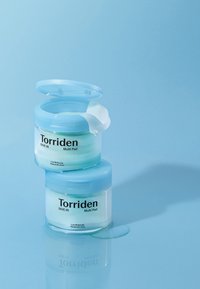 To klare glasbeholdere med Torriden Multi Pad stablet oven på hinanden, med blå låg og lys grøn indhold, hvor en fugtig pad stikker op fra den øverste beholder.