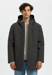 Giacca nera con cappuccio realizzata in materiale leggero e liscio. Presenta una chiusura con zip frontale, tasche laterali e una vestibilità rilassata con maniche lunghe.