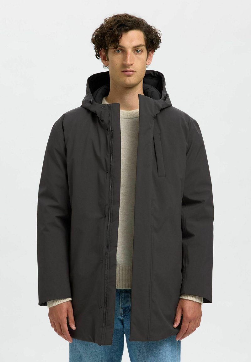 Giacca nera con cappuccio realizzata in materiale leggero e liscio. Presenta una chiusura con zip frontale, tasche laterali e una vestibilità rilassata con maniche lunghe.