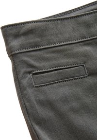 Sivá rifľovina s hladkou textúrou. Má zadné vrecko s obdĺžnikovým otvorom a kontrastné prešívanie pozdĺž švov.