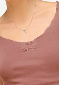 Cou du cou et haut de la poitrine portant un collier en argent avec un pendentif en forme de "B", et un top sans manches mauve avec des détails de tissu froncé.