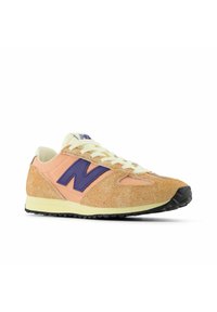 Scarpa da ginnastica arancione e panna con logo "N" viola, parte superiore in camoscio lavorato, lacci crema e suola in gomma nera.