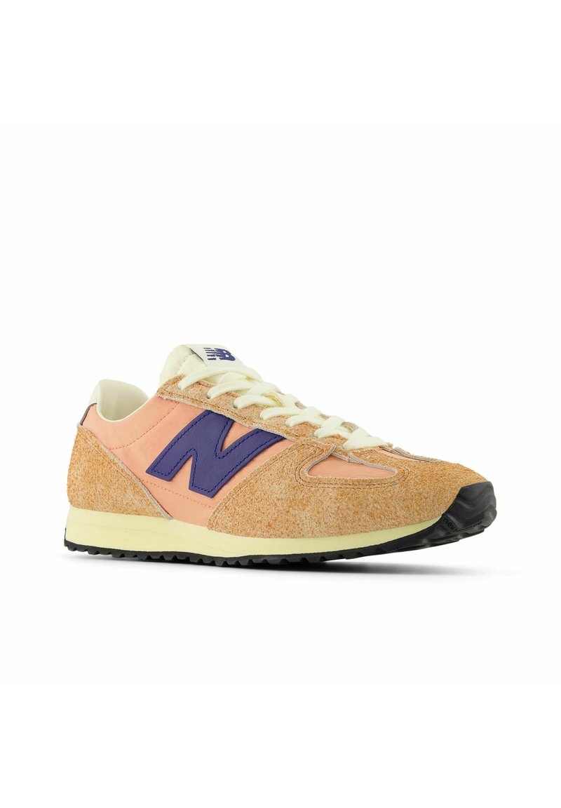Orange och krämfärgad sportig sneakersko med en lila "N"-logotyp, texturerad mockaöverdel, krämfärgade snören och svart gummisula.