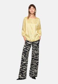 Satin yellow blouse with a round neckline and three-quarter puff sleeves, paired with high-waisted black and white zebra print trousers.