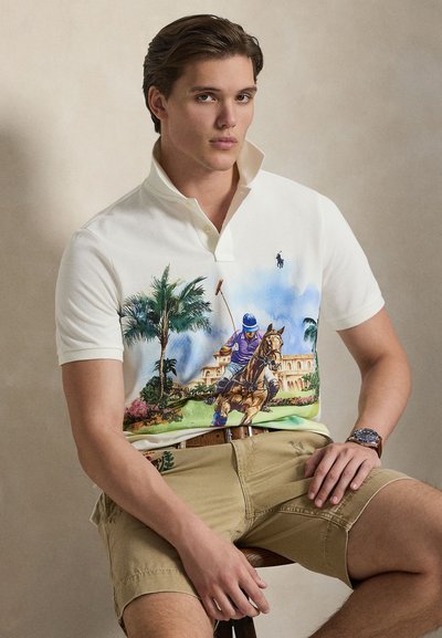 Balta polo krekls ar krāsainu zirgu polo apdruku, īsām piedurknēm, trīs pogu aizdari un nelielu logotipu uz krūtīm. Valkāts kopā ar haki šortiem.