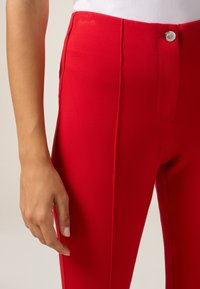 Rode aangesloten broek met een gladde textuur, hoge taille en een zilveren knoopsluiting. Heeft zijschoenen en een slanke silhouette.