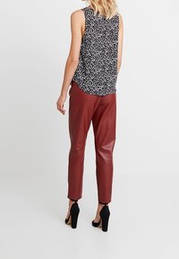 Černobílý vzorovaný top bez rukávů spojený s vínovými koženými kalhotami s úzkými nohavicemi a černými lodičkami na vysokém podpatku.