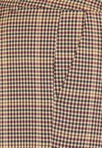 Geweven stof met een ruitpatroon in beige, zwart en bordeauxrood. Bevat kleine, uniforme vakjes en een gladde textuur met een minimale glans.