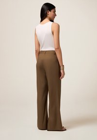 Bruine wijde broek met een gladde textuur, geplooide voorkant en achterzakken, gecombineerd met een effen witte mouwloze top.