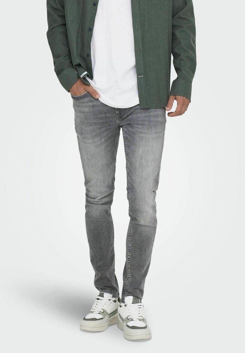 Jeans in denim grigio con vestibilità slim, design sbiadito e dettagli di sfumatura leggeri. Abbinati a una t-shirt bianca e una camicia verde a bottoni.