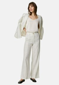 Vitrandig kostymset med en skräddarsydd kavaj och vida byxor, i kombination med en ljus linne och svarta ballerinas. Slät tygtextur.