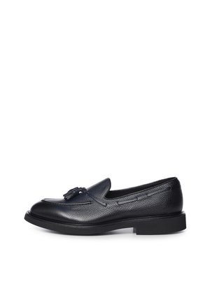 Mocasín negro de piel granulada con detalles de borlas y un tacón bajo y grueso, sobre fondo blanco.