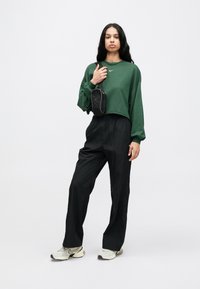 Πράσινο κοντό φούτερ, μαύρο φαρδύ παντελόνι και ανοιχτό γκρι αθλητικά παπούτσια. Μικρή μαύρη τσάντα φορεμένη χιαστί. Απλή, καθημερινή εμφάνιση.