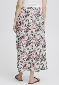 Jupe maxi fleurie avec une taille élastique, à base blanche et imprimé botanique vibrant en rose et vert. Le matériau semble léger et fluide.