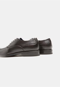 Scarpe in pelle nera con una texture liscia, punta arrotondata e cuciture sottili. Presentano un tacco basso impilato e lacci piatti.