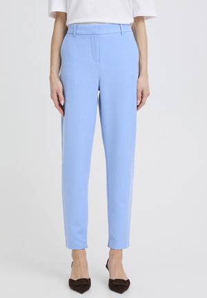 Jasnoniebieskie, dopasowane spodnie o gładkiej fakturze, wąskim kroju i subtelnych kantach; zestawione z ciemnobrązowymi, szpiczastymi butami.