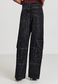 Pantaloni cargo neri a gamba larga in denim sbiadito con tasche multiple, cuciture visibili e rifinitura pulita all'orlo.