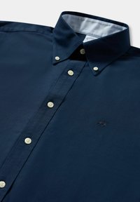 Camicia blu navy con bottoni bianchi e logo ricamato sul petto, con collo con bottoni e fodera interna del collo chiara.