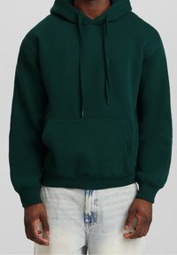 Grön huvtröja i tjockt material, med en framficka, snoddar och ribbade ärmslut och nederkant. Bärs med ljusblå jeans.