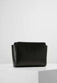 Borsa a mano in pelle nera con un design strutturato, caratterizzata da una texture liscia e un'estetica minimalista, posta su uno sfondo bianco uniforme.