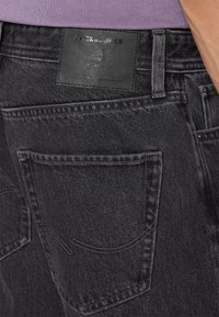 Jeans de mezclilla negra con una superficie texturizada, detalle en la etiqueta trasera y dos bolsillos traseros con costuras curvas.