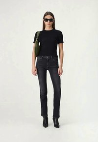 Svart t-skjorte, høyt liv i mørke jeans og svarte ankelstøvler. Tilbehør: grønn skulderveske og firkantede solbriller. Enkelt, tettsittende design.