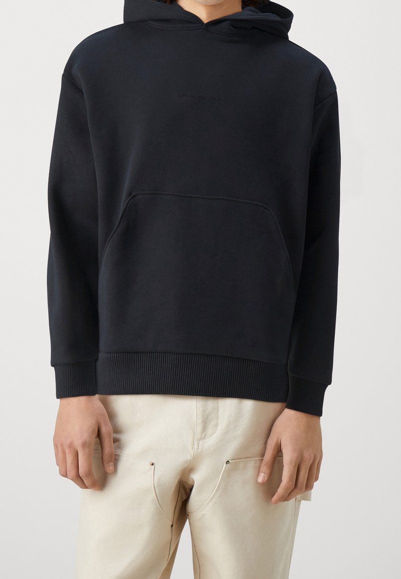 Sweat-shirt à capuche noir en tissu doux, avec une poche kangourou, des poignets et un ourlet côtelés. Design minimaliste sans logo visible.
