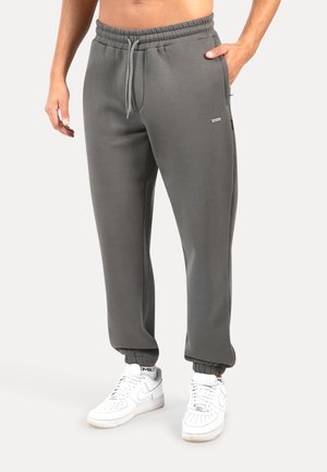 Pantalones de chándal grises con cinturilla elástica y cordón, que cuentan con bolsillos laterales y pantalones con puños, combinados con zapatillas blancas.