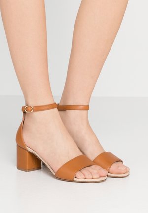 Sandalias de cuero marrón con tacón bloque, diseño de puntera abierta, correa en el tobillo y textura lisa. El tacón es grueso y de forma cuadrada.