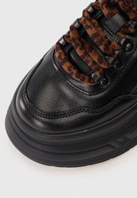 Black leather sneaker featuring a textured surface, leopard-print laces, and a chunky black sole with visible cushioning.