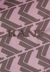 Tekstilinis audinys, pasižymintis ryškiu geomtriniu raštu tamsiai rudos ir rožinės spalvos. Išsiuvinėtas "KANI" logotipas tamsesnėmis siūlėmis. Lygus paviršius.