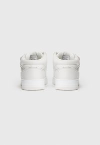 Fehér bőr sneaker cipők, alacsony szárú kialakítással, kerek orral, párnázott nyakkal és mintás gumi talppal. Címkék láthatók a cipők belsejében.