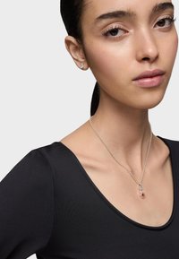 Collar de plata con un colgante rojo, llevado sobre una blusa negra. El colgante presenta una pequeña piedra redonda y detalles de diseño intrincados.