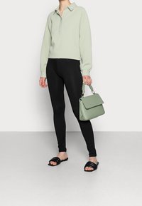 Pull léger vert texturé, leggings noirs, sandales plates noires et un petit sac à main vert avec une poignée tressée.