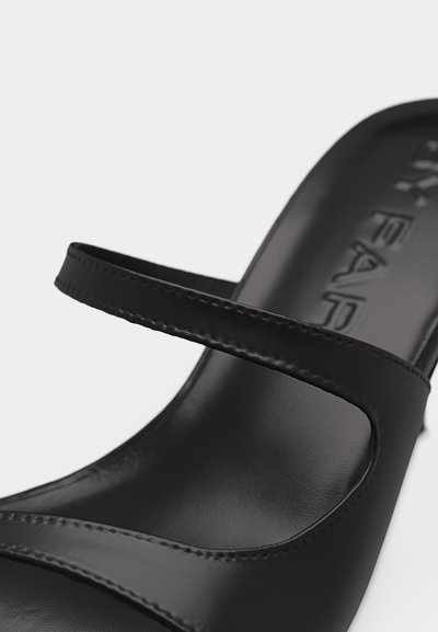 Sandale en cuir noir avec deux fines lanières sur le pied et une semelle intérieure lisse, légèrement rembourrée, avec un logo embossé.