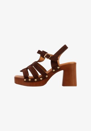 Sandale compensée en daim marron avec talon bloc, plusieurs brides, clous dorés le long de la semelle et fermeture à boucle réglable.