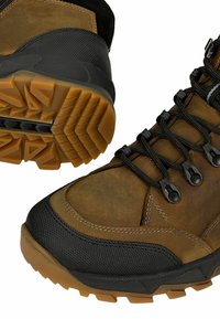 Brązowe i czarne buty hikingowe z teksturowaną tkaniną, gumowym noskiem i solidną podeszwą z bieżnikiem. Posiadają sznurowany design i ozdobne przeszycia.