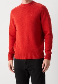 Roter Strickpullover mit langen Ärmeln, geripptem Ausschnitt und Saum. Hergestellt aus weichem Material, mit einem dezenten Logodetail auf der Brust.