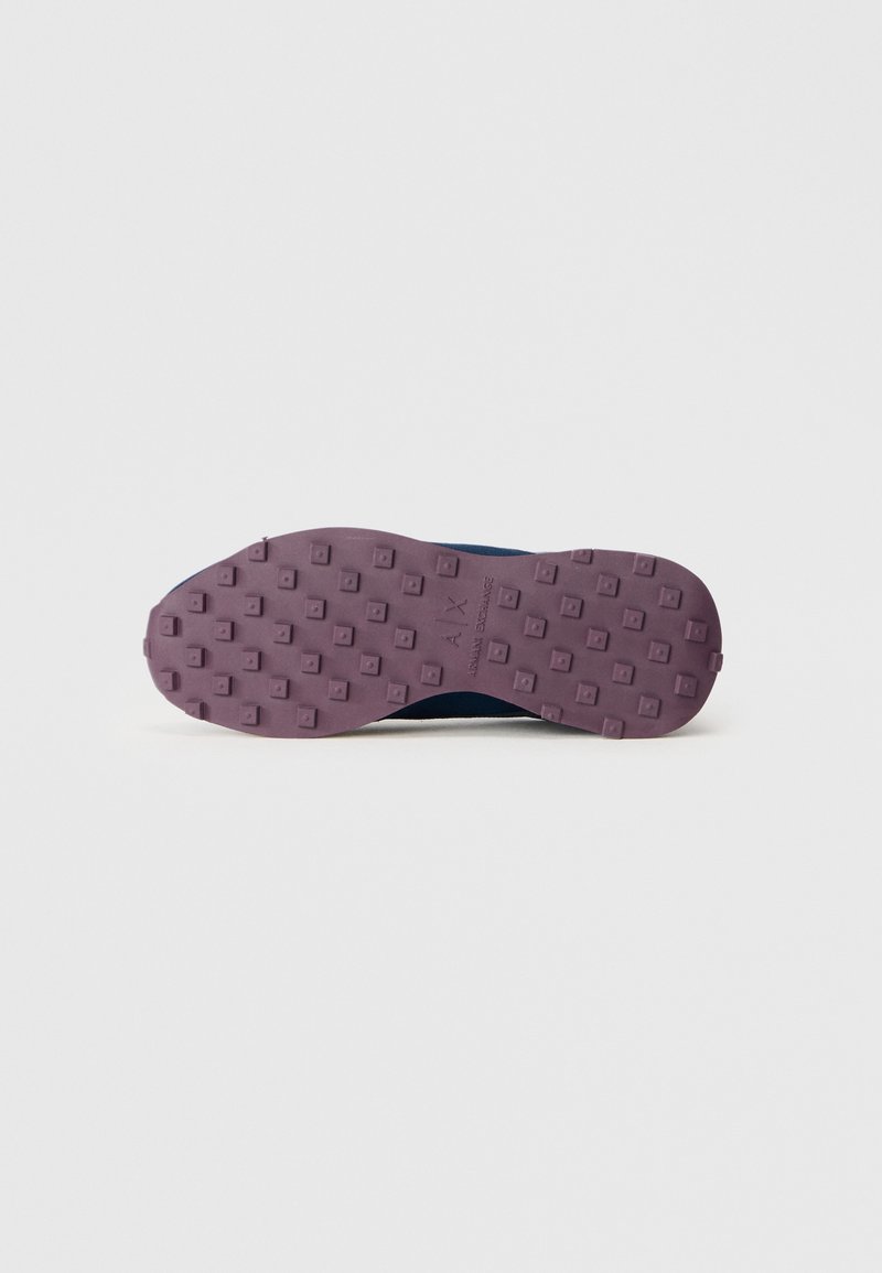 Semelle de chaussure avec un profil en caoutchouc violet présentant des clous carrés et le logo "A|X Armani Exchange" au centre sur un fond blanc.