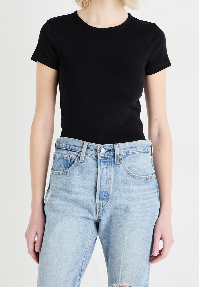 Svart åtsittande t-shirt med rundad halsringning och korta ärmar, i kombination med ljusblå hög midja jeans med slitna detaljer.