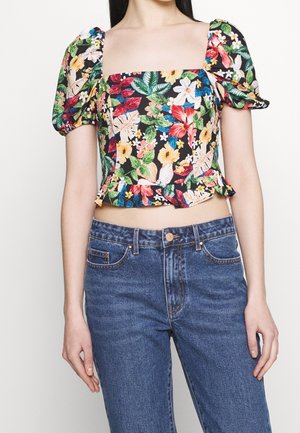 Bloemen crop top met pofmouwen, zwarte achtergrond, met kleurrijke bloemen en bladeren; gedragen met een high-waisted blauwe spijkerbroek.