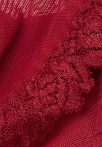 Czerwona koronkowa tkanina z teksturowanym wzorem kwiatowym na drobnym siatkowym tle. Materiał wydaje się delikatny i misterny.