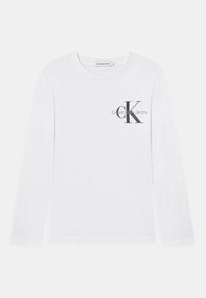 Chemise blanche à manches longues Calvin Klein Jeans avec logo noir "cK" et nom de marque imprimés sur le côté gauche de la poitrine.