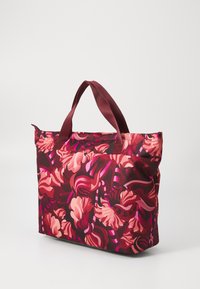Sac fourre-tout à motifs floraux dans des tons de rouge et de rose, avec des poignées robustes et un design spacieux, sur fond blanc.