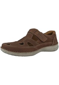 Brown leather shoe with cut-out sections, hook-and-loop strap, contrast stitching, round toe, and a textured rubber sole.