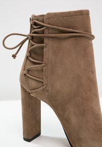 Bottine en daim marron avec un talon bloc haut et des lacets décoratifs croisés noués à l'arrière.