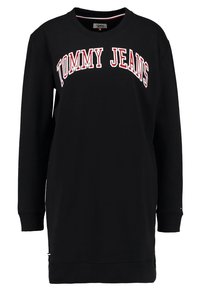 Black sweatshirt dress featuring "TOMMY JEANS" logo in red and white arch text. Long sleeves and ribbed cuffs. Simple, unadorned design.